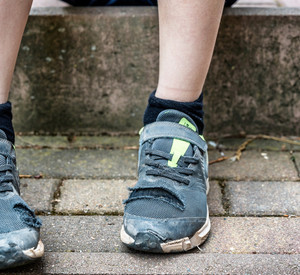 Unkenntliches Kind sitzt mit kaputten Schuhen auf Gehweg