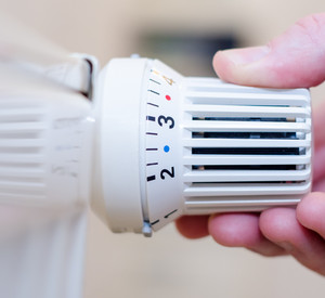 Eine Hand dreht am Drehregler eines Heizkörpers